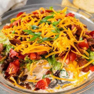 Cold BLT dip with cream cheese in glass pie plate with some removed to show layers.