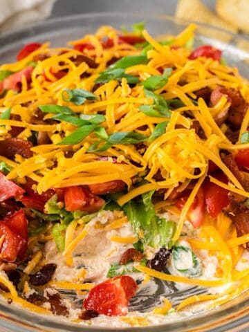 Cold BLT dip with cream cheese in glass pie plate with some removed to show layers.