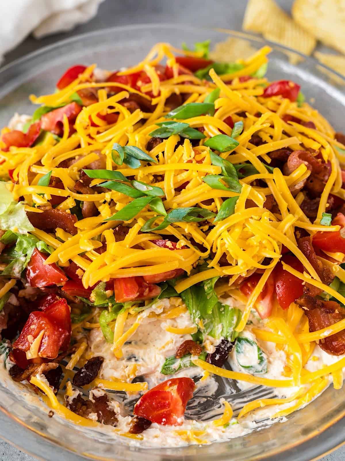 Cold BLT dip with cream cheese in glass pie plate with some removed to show layers.