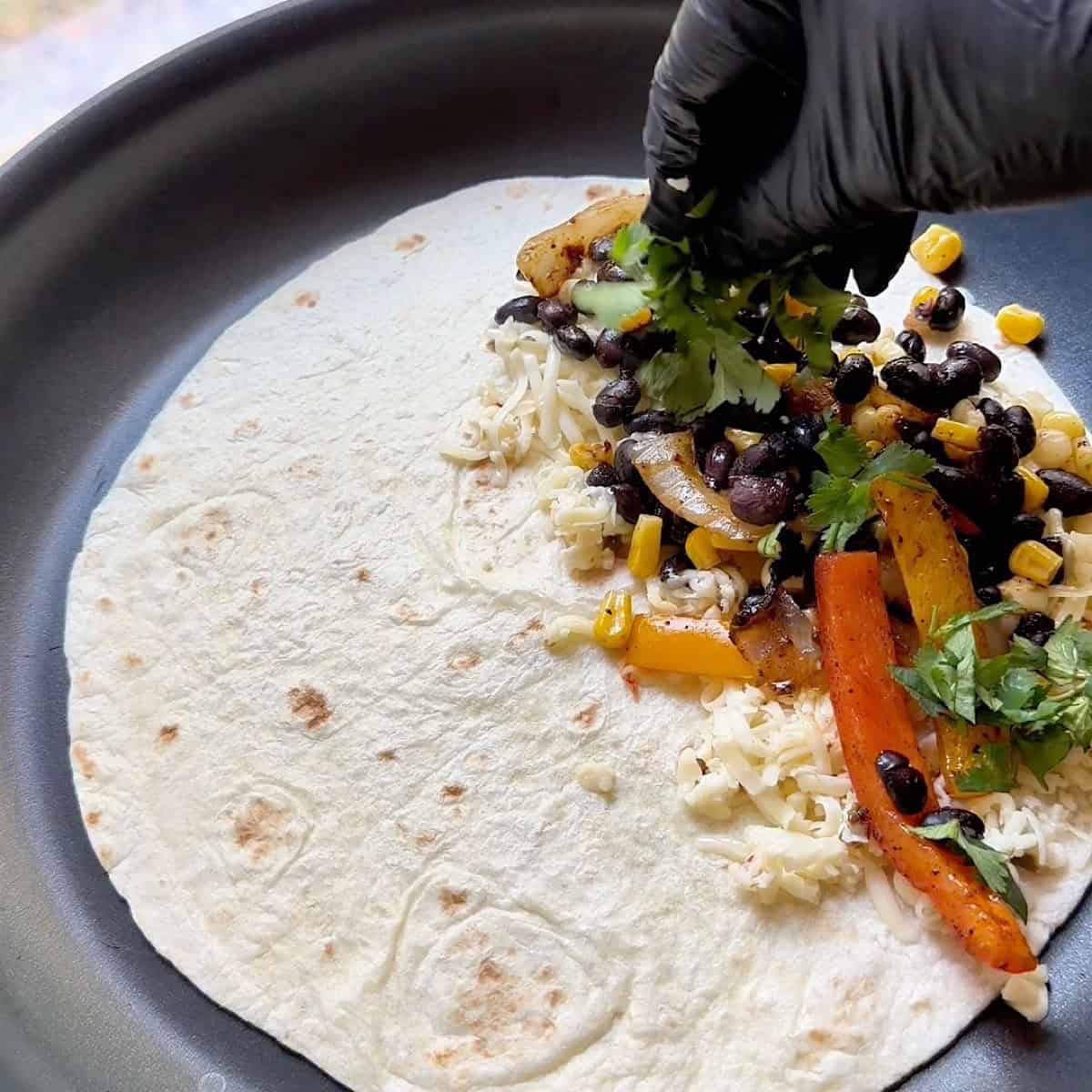Open tortilla in a non stick skillet with vegetable mixture and cheese covering half.