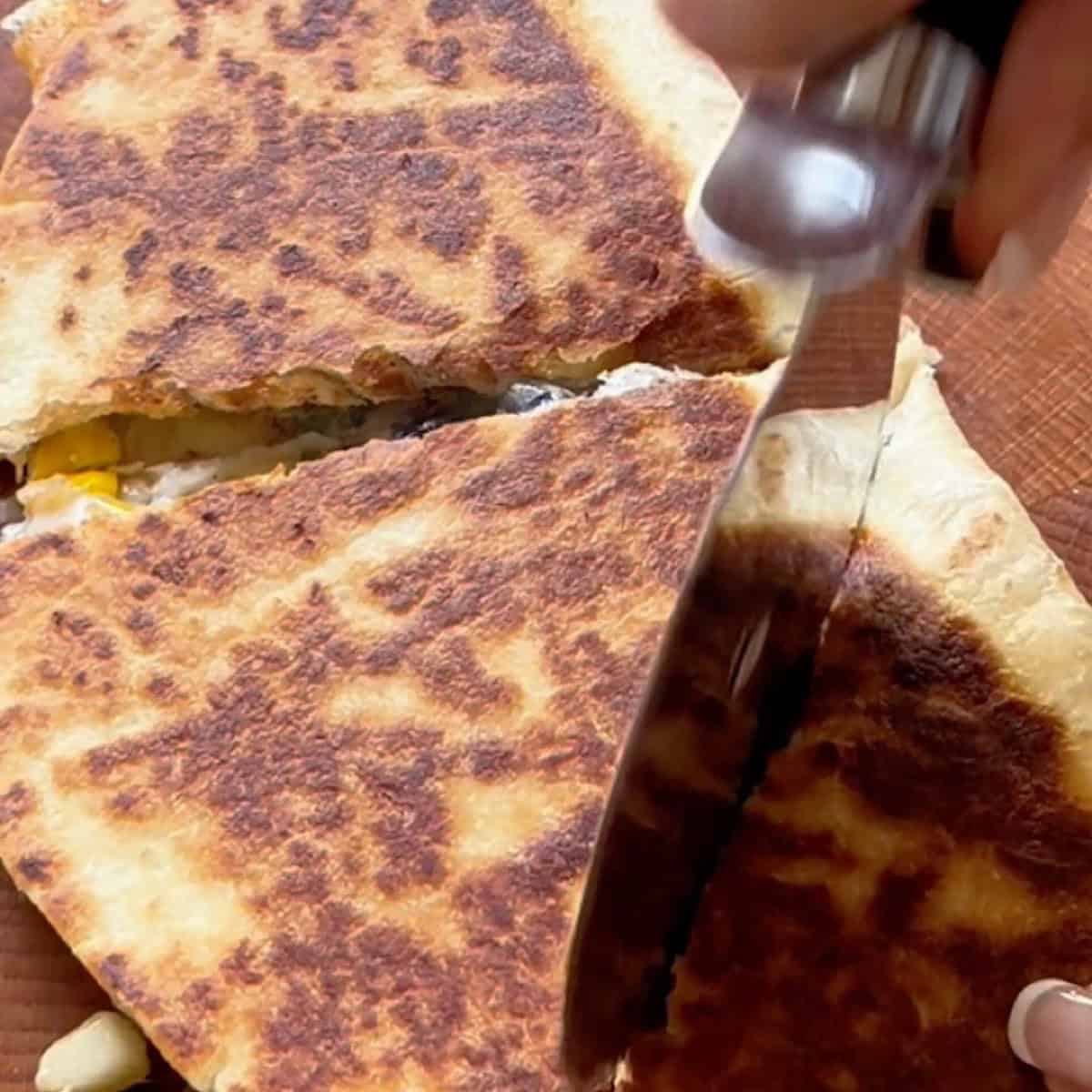 Pan fried vegetarian quesadilla on cutting board cut into wedges.