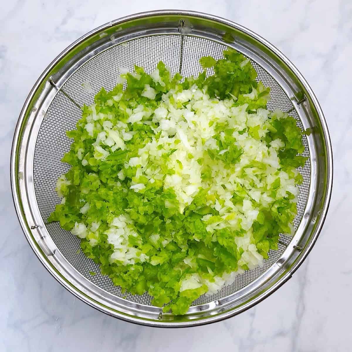 Bell pepper and onion draining in a colander.