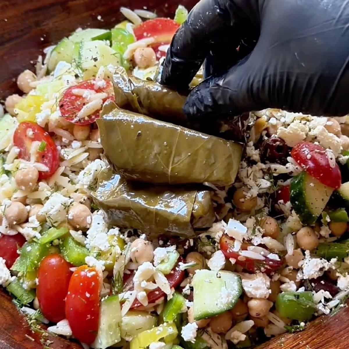 Placing dolmades on top of prepared orzo salad.