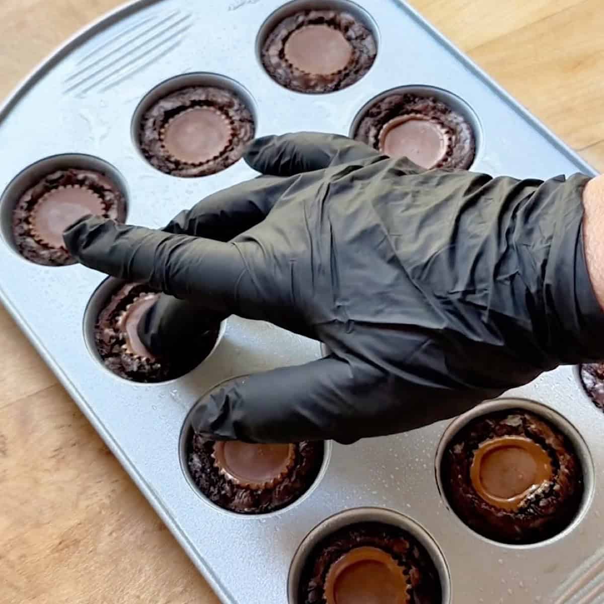 Gently pressing a frozen peanut butter cup into the warm brownies.