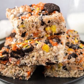 Halloween Rice Krispie treats stacked on a plate beside milk and linen.