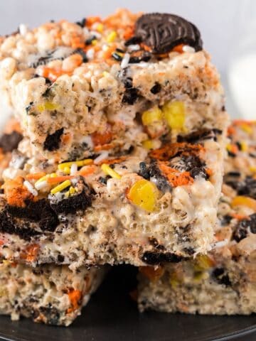 Halloween Rice Krispie treats stacked on a plate beside milk and linen.