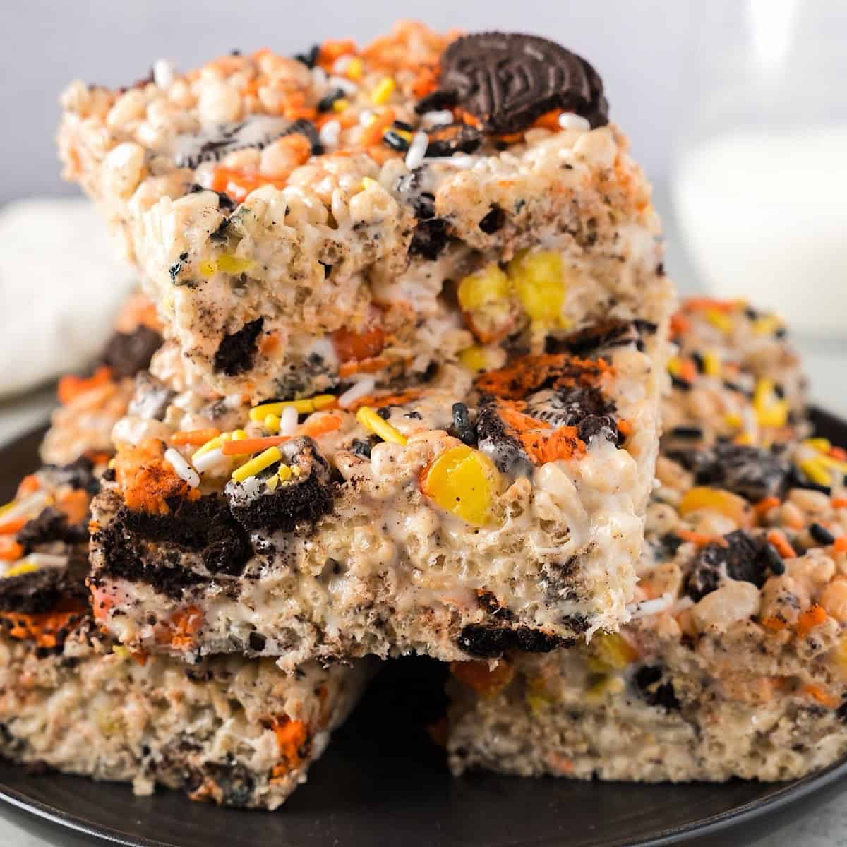 Halloween Rice Krispie treats stacked on a plate beside milk and linen.