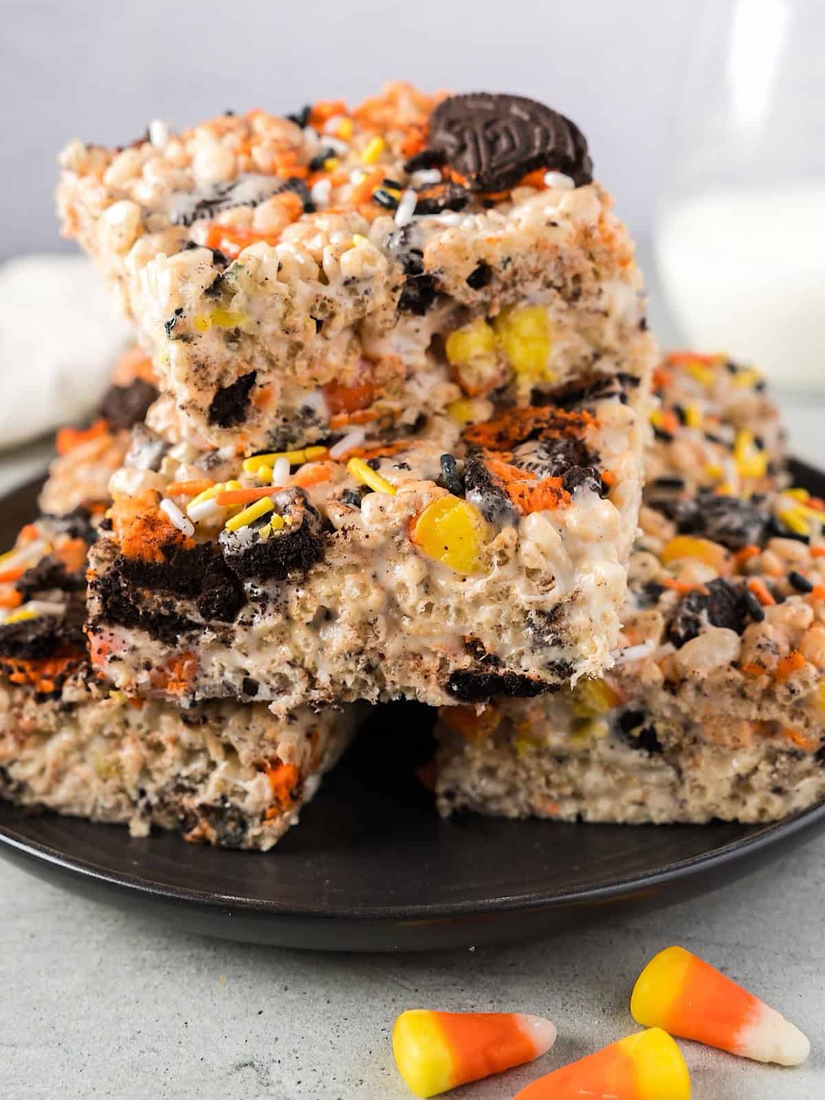 Halloween Rice Krispie treats stacked on a plate beside milk and linen.