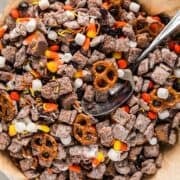 Halloween snack mix in a bowl with spoon next to a fall linen.