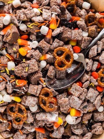 Halloween snack mix in a bowl with spoon next to a fall linen.