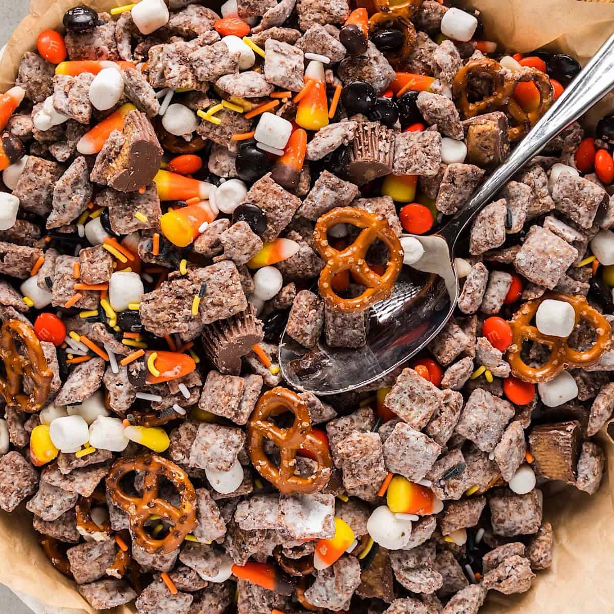 Halloween snack mix in a bowl with spoon next to a fall linen.