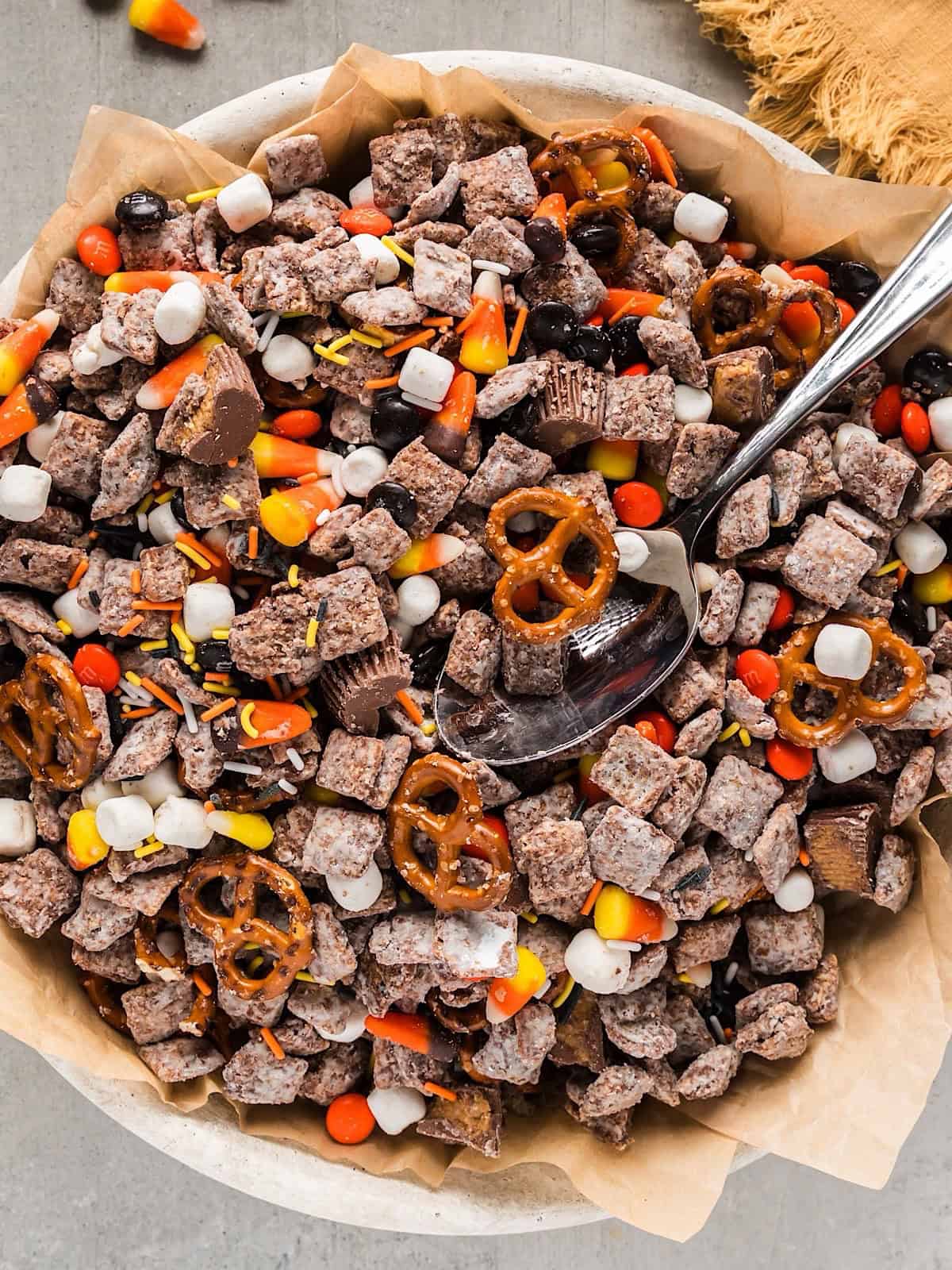 Halloween snack mix in a bowl with spoon next to a fall linen.