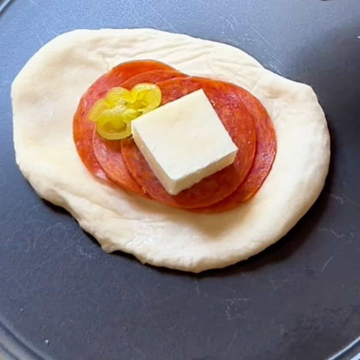 One flattened roll with pepperoni, cheese, and pepperoncini pepper.