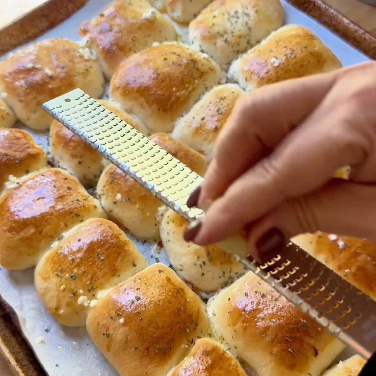 Applying seasoning and parmesan to baked pepperoni rolls.