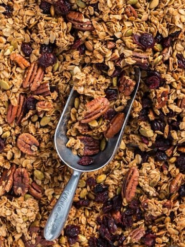 Maple pecan granola on a sheet pan with a metal scoop.