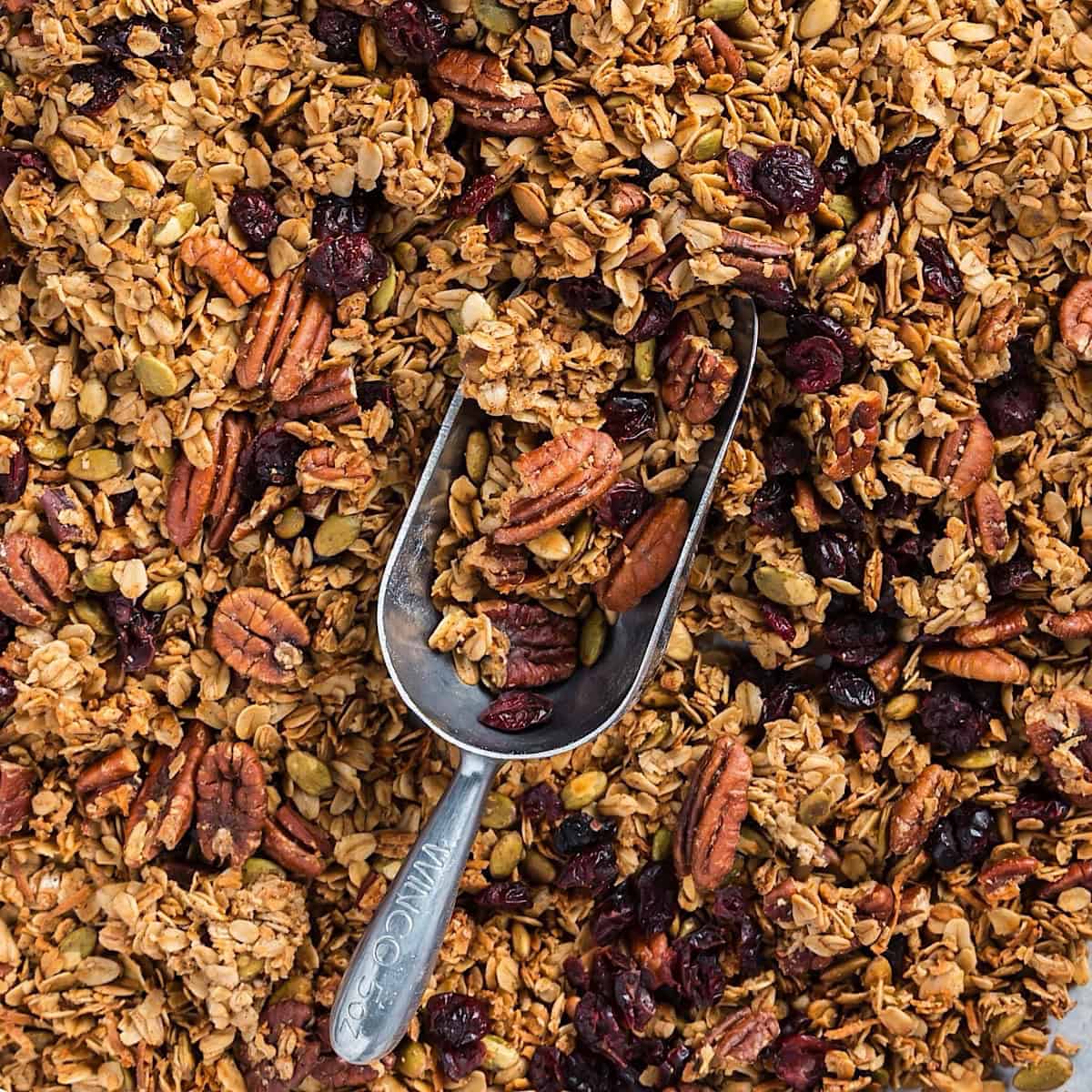 Maple pecan granola on a sheet pan with a metal scoop.