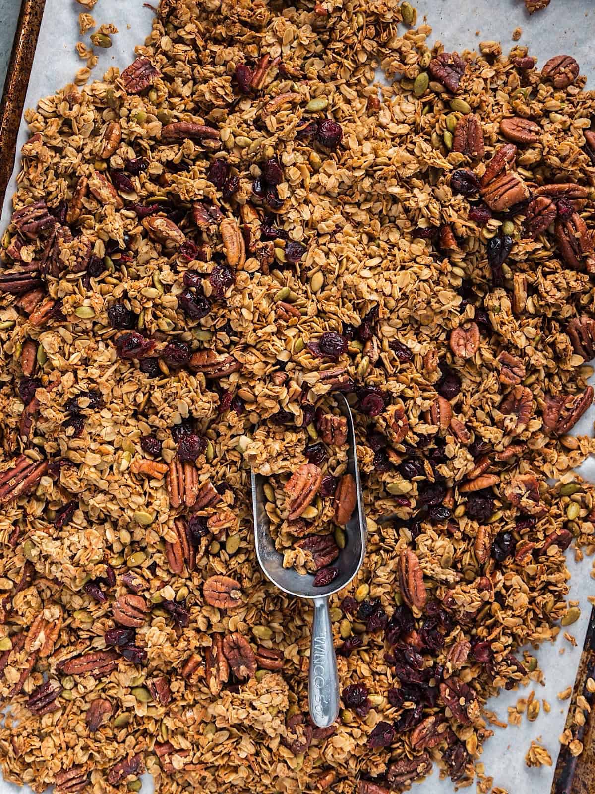 Maple pecan granola on a sheet pan with a metal scoop.