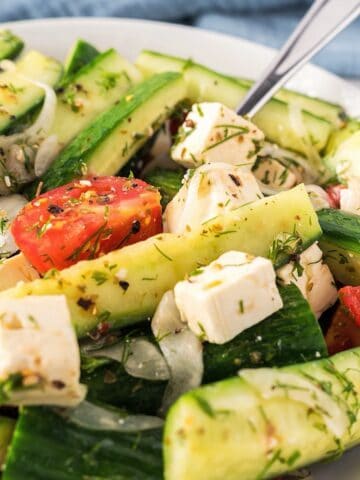 Mediterranean Cucumber and Tomato Salad in a white bowl with fork and blue linen in background.