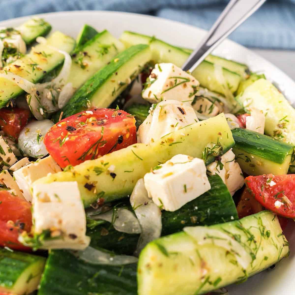 Mediterranean Cucumber and Tomato Salad in a white bowl with fork and blue linen in background.