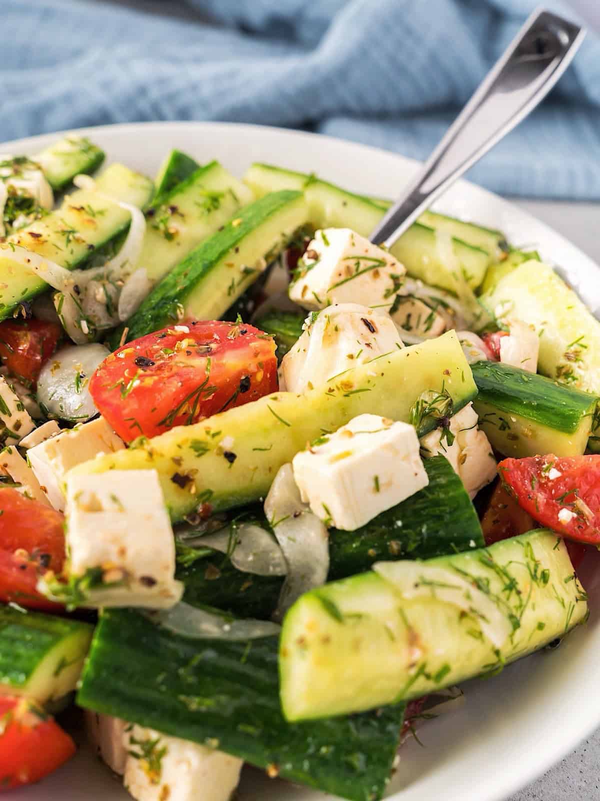 Mediterranean Cucumber and Tomato Salad in a white bowl with fork and blue linen in background.