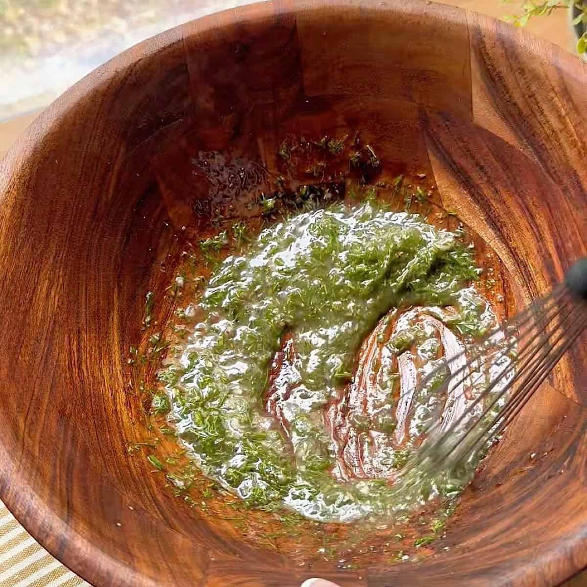 Whisking the red wine vinaigrette salad dressing with fresh herbs in a wooden salad bowl.