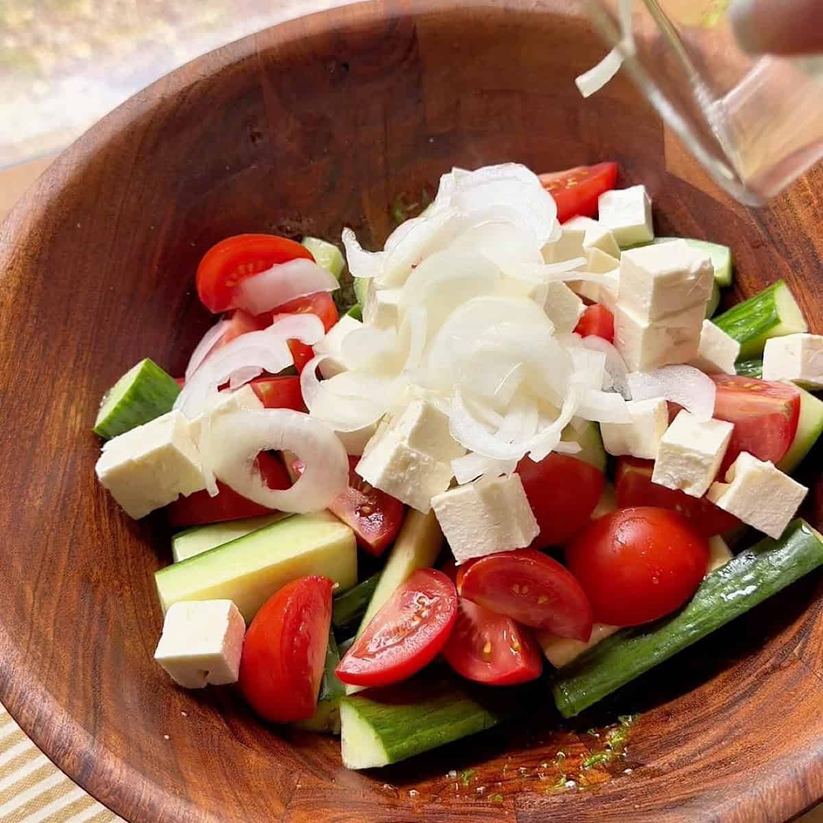 Adding the vegetables and feta cheese to the dressing.