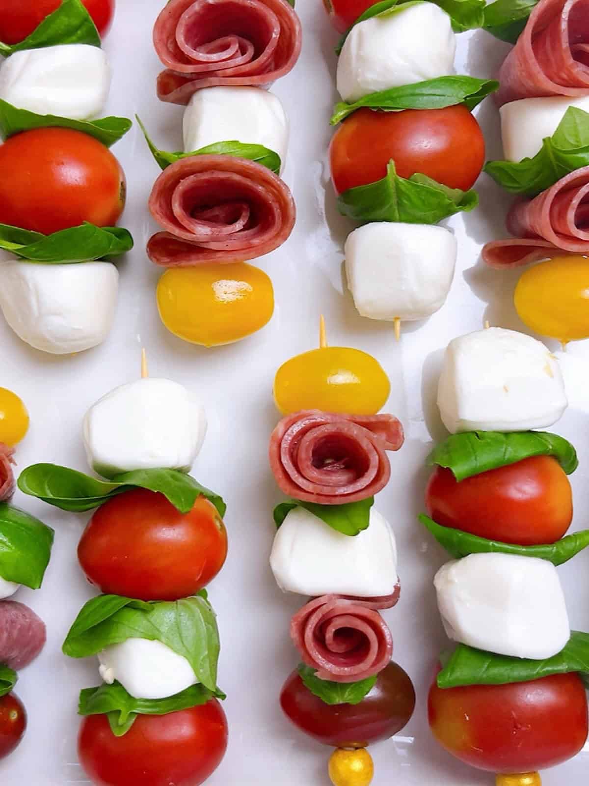 Mini caprese skewers with salami roses lined up on a platter.