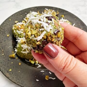 Holding a chilled and coated pistachio energy ball above plate of remaining energy bites.