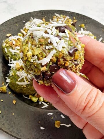 Holding a chilled and coated pistachio energy ball above plate of remaining energy bites.
