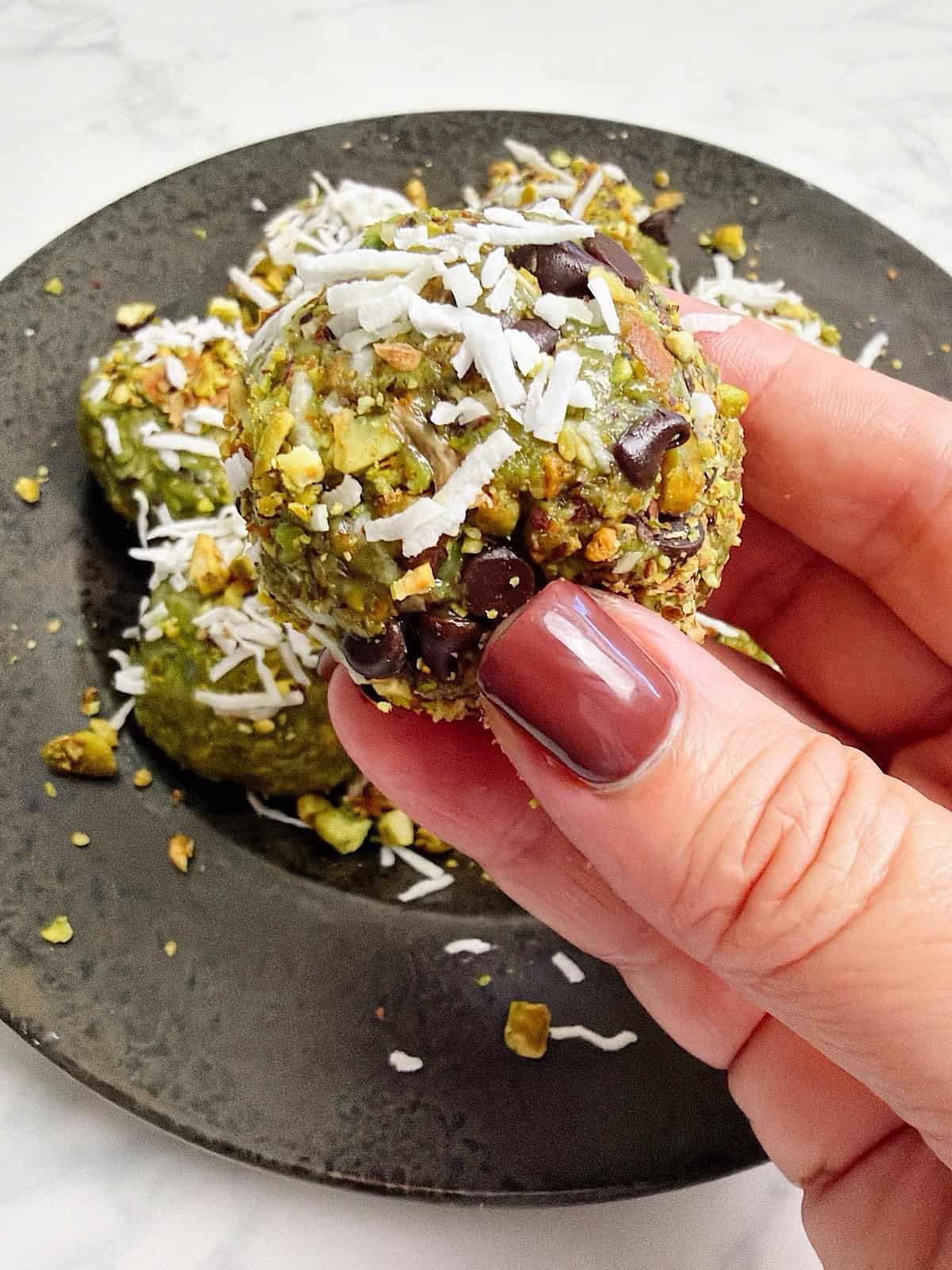 Holding a chilled and coated pistachio energy ball above plate of remaining energy bites.