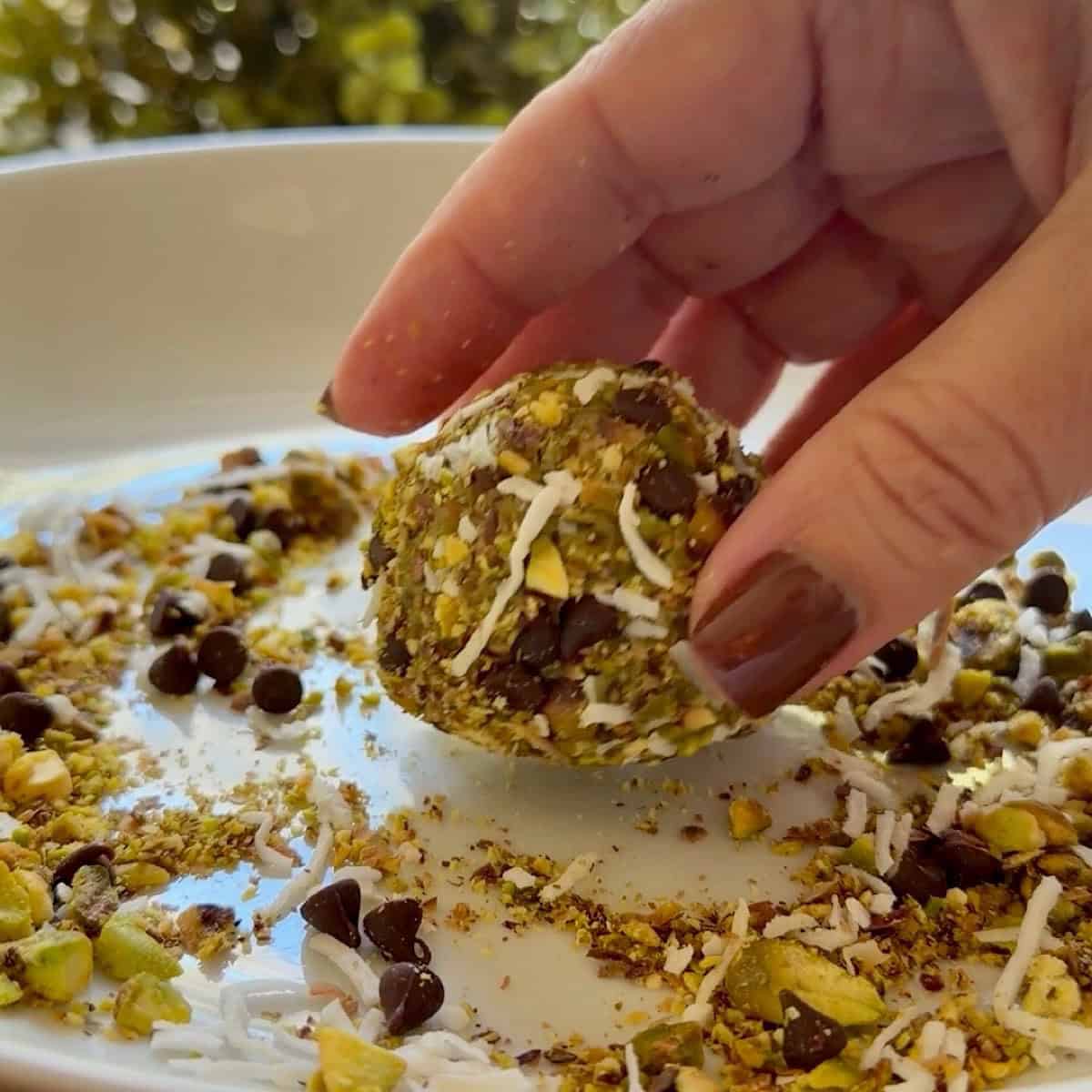 Rolling and coating a pistachio energy ball in coconut, chocolate, chips and crushed pistachios.