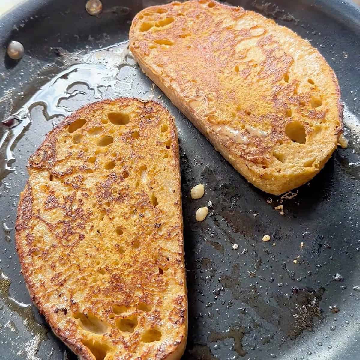 Two browned french toast slices in a skillet with butter.