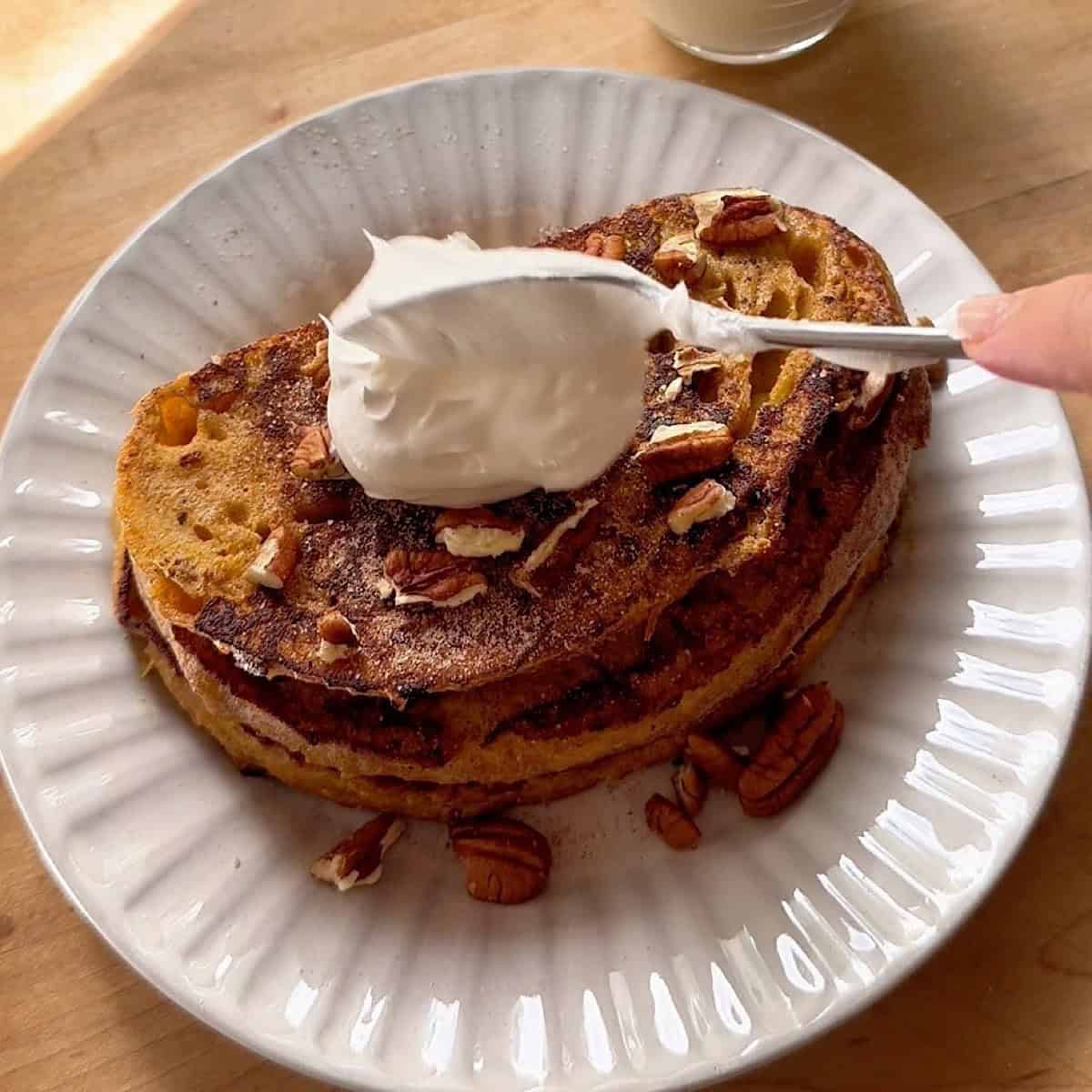 Pumpkin spice french toast stacked with cinnamon sugar, pecans, and whipped cream.