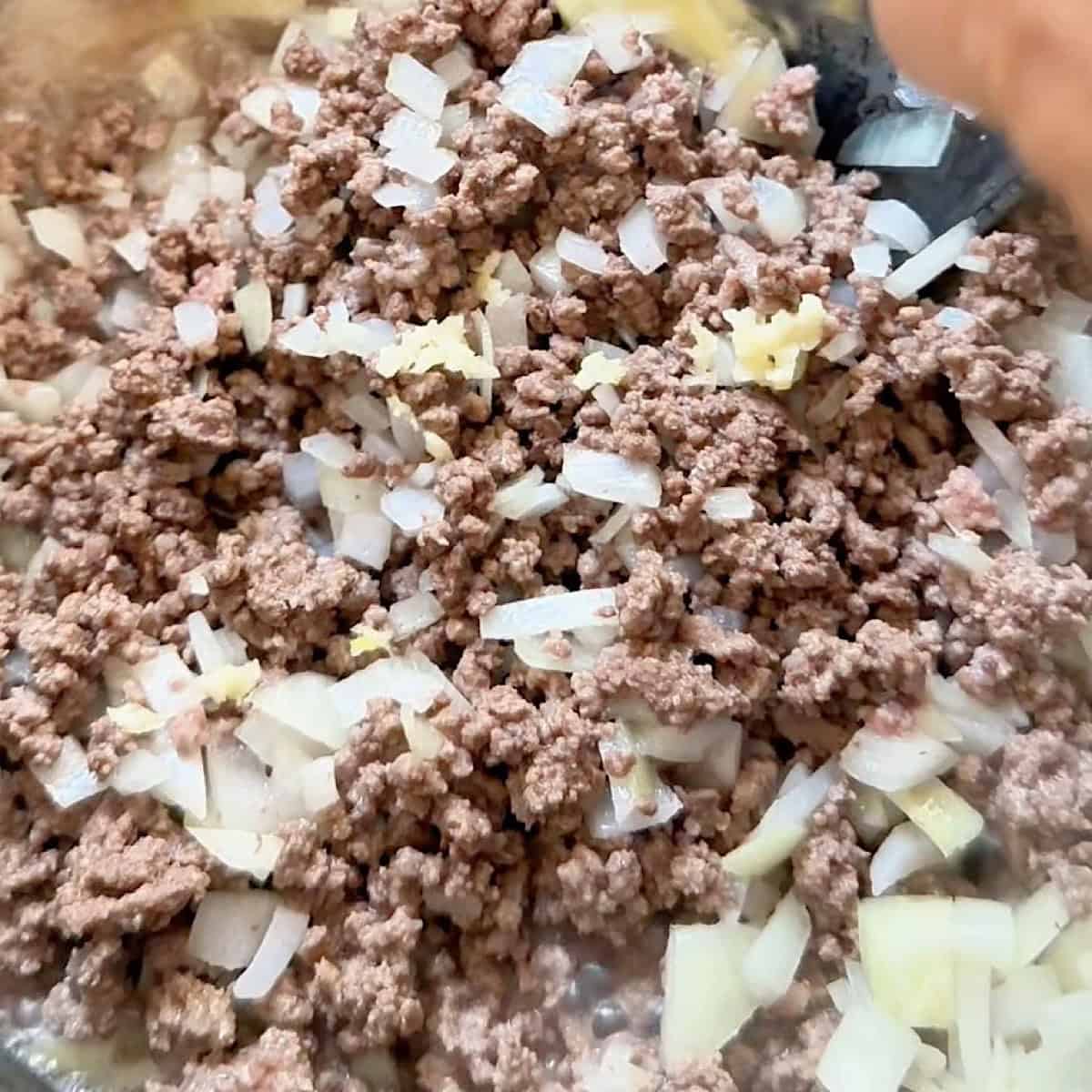 Adding minced garlic to ground beef and onions.