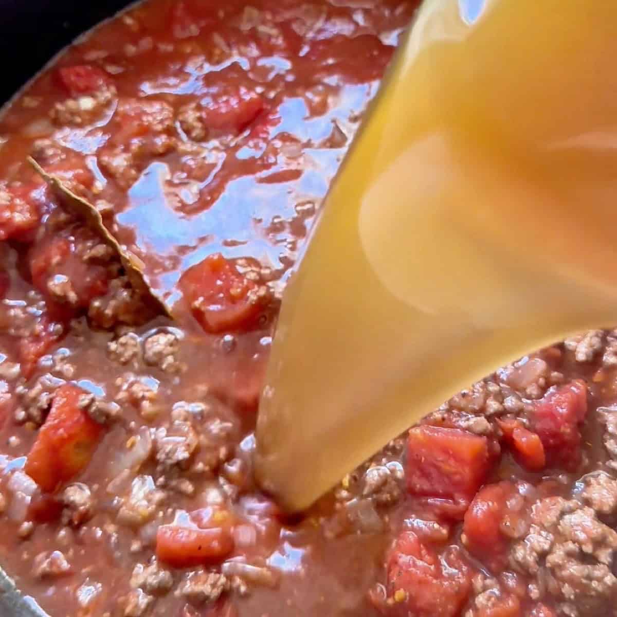 Pouring beef broth into the tomato ground beef base.