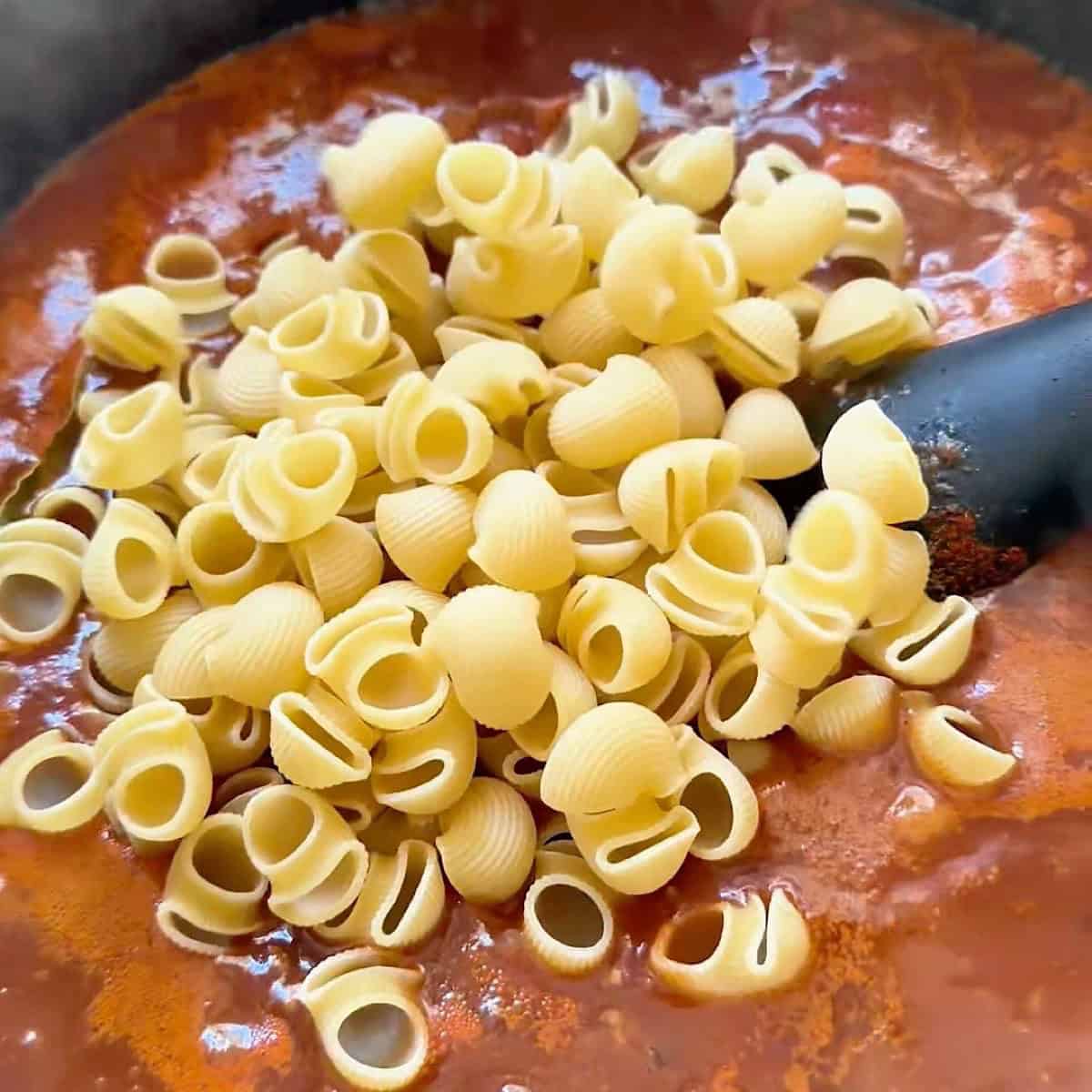 Adding pasta to the tomato ground beef base.