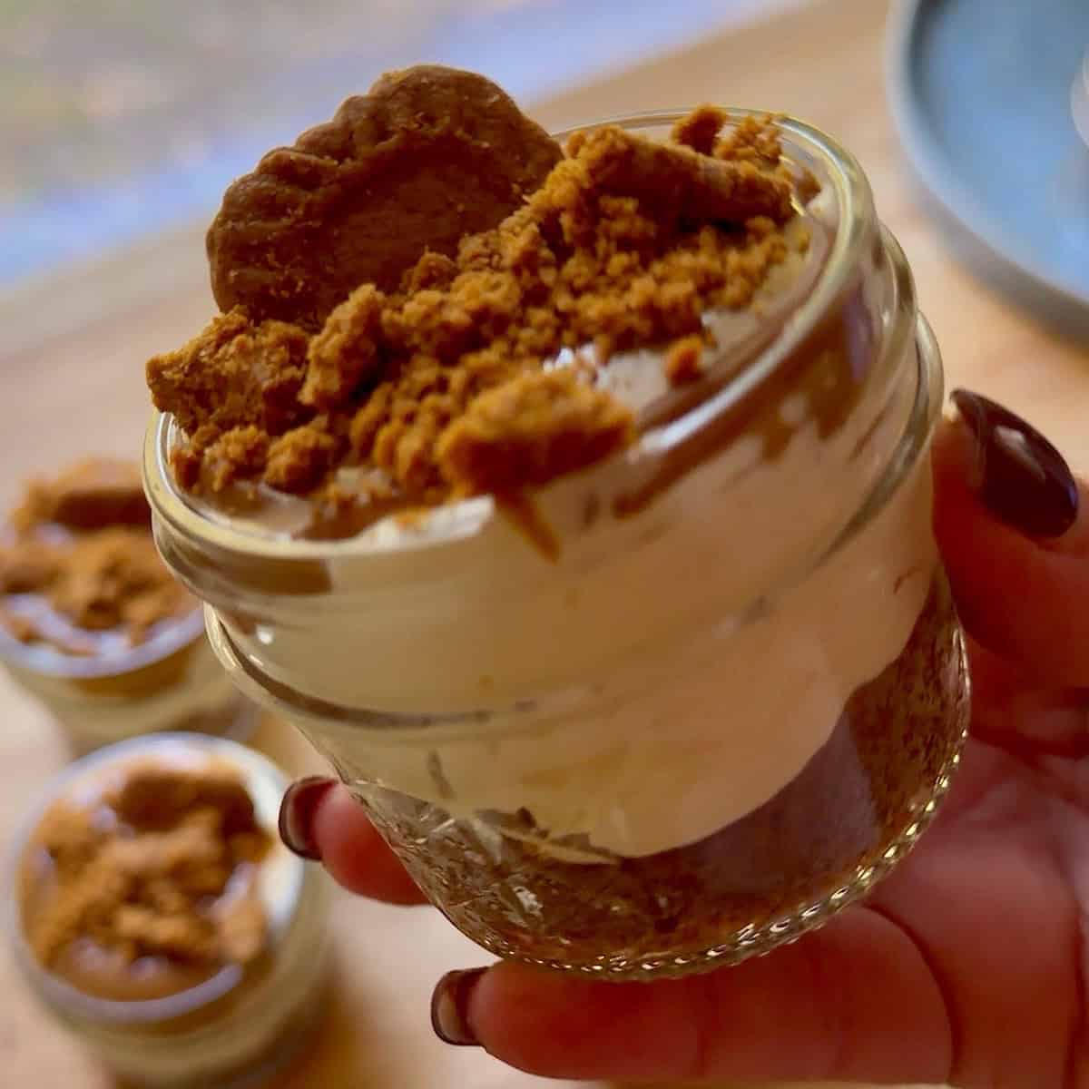 Holding a Biscoff cheesecake cup with a cookie crumb garnish.