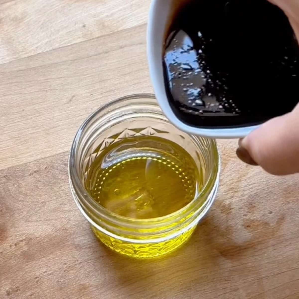 Pouring balsamic vinegar into extra virgin olive oil to make the balsamic vinaigrette.
