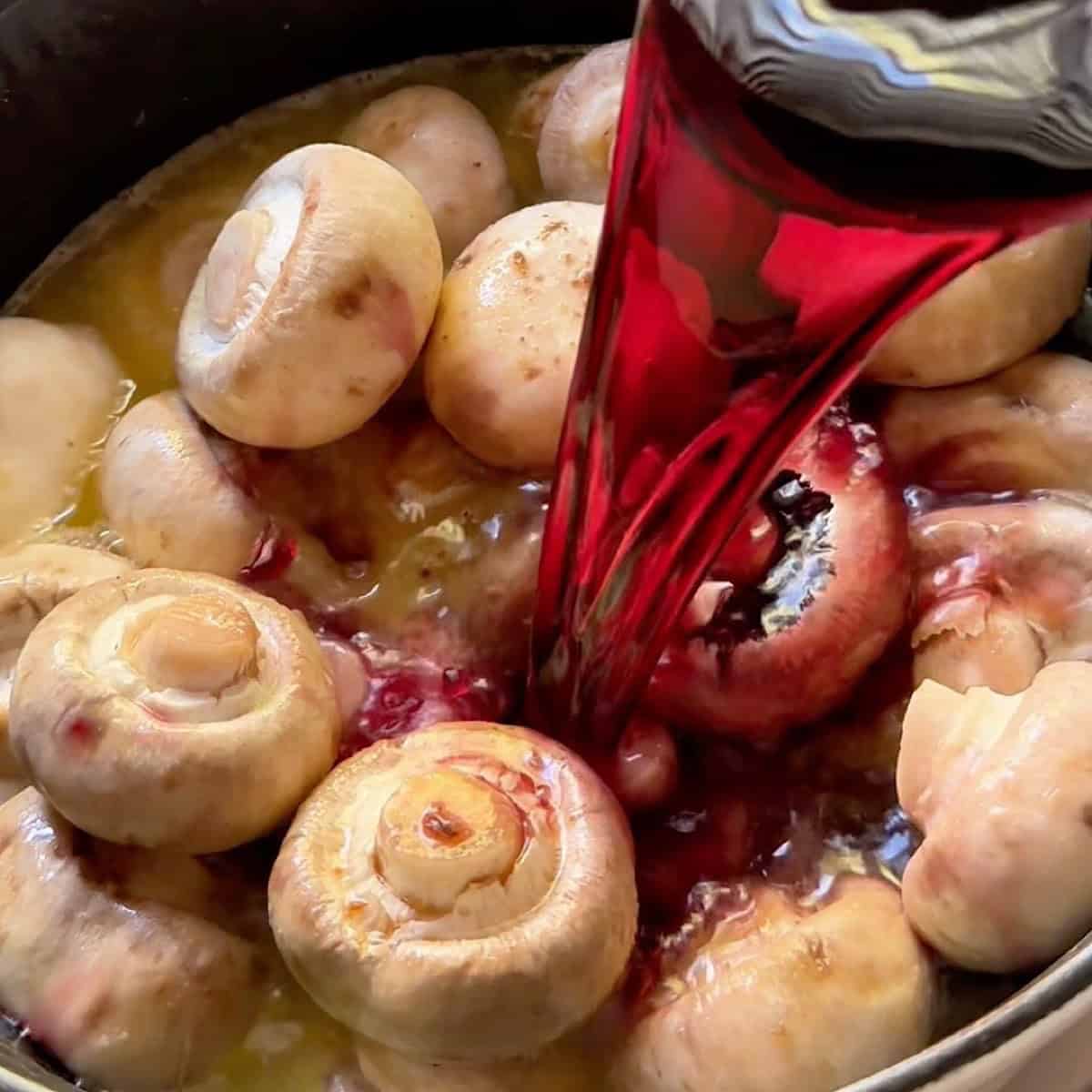 Adding red wine to the beef both and mushrooms.