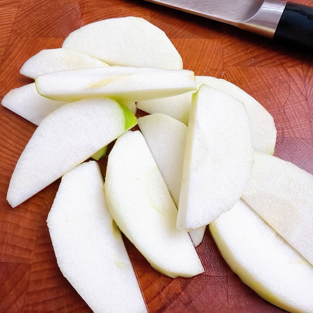 Sliced grannysmith apples on a cutting board beside a knife.