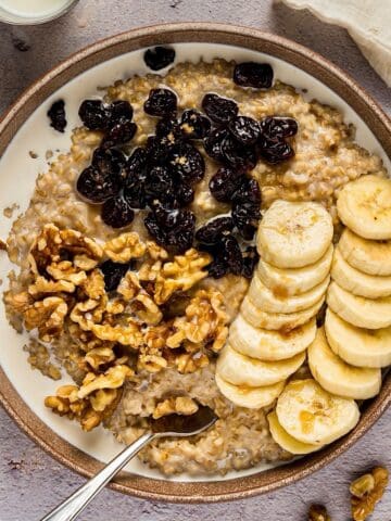 Creamy Instant Pot steel cut oats in bowl with toppings and linen nearby.