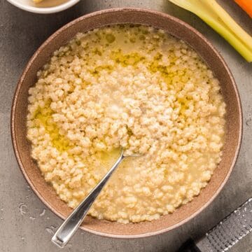 Pastina Soup in a bowl with spoon topped with a drizzle of olive oil and parmesan.