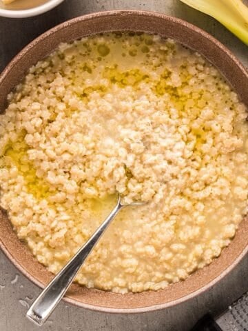 Pastina Soup in a bowl with spoon topped with a drizzle of olive oil and parmesan.