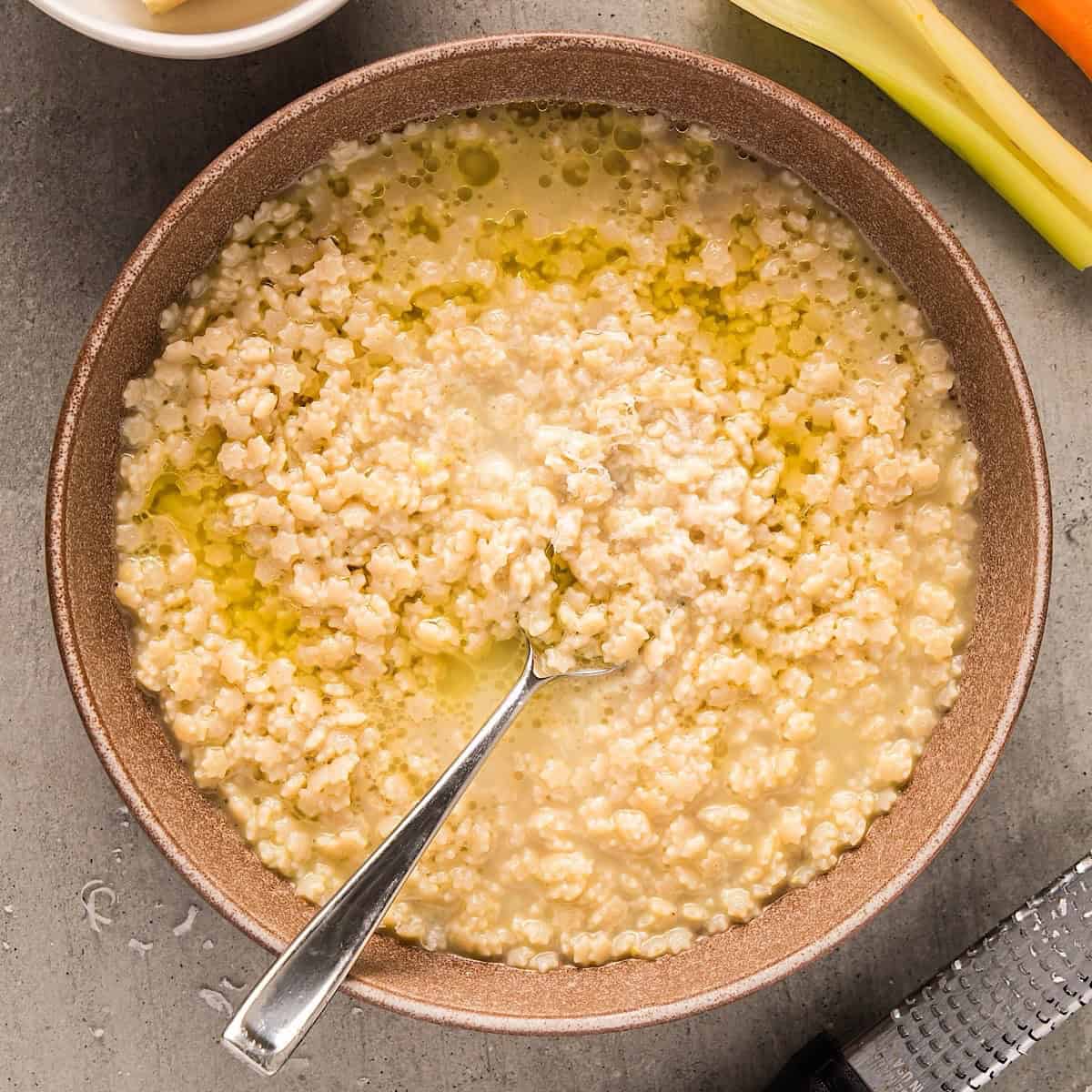 Pastina Soup in a bowl with spoon topped with a drizzle of olive oil and parmesan.