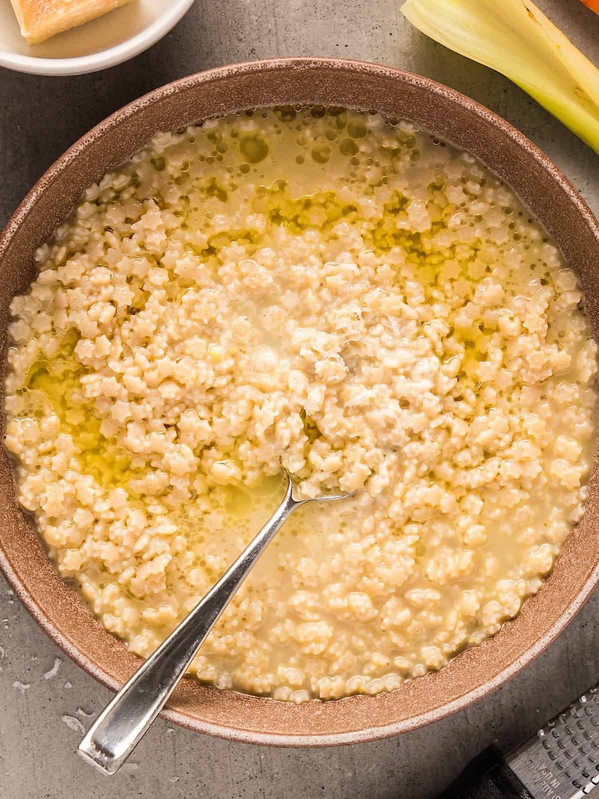 Pastina Soup in a bowl with spoon topped with a drizzle of olive oil and parmesan.