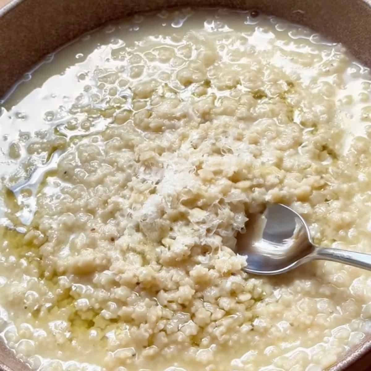 Pastina in a bowl with melted butter, oil, and grated parmesan cheese.