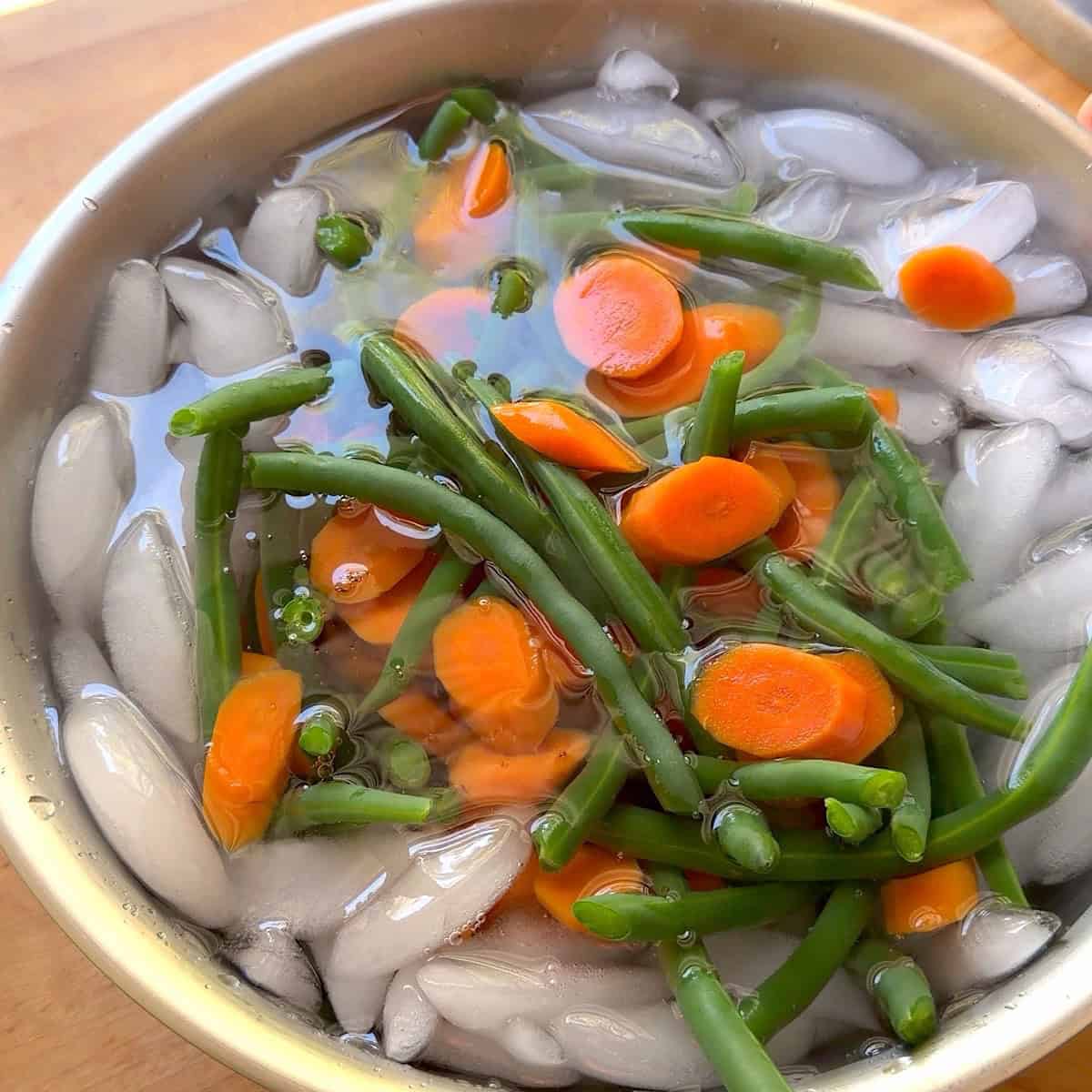 Blanched green beans and carrots in ice water.
