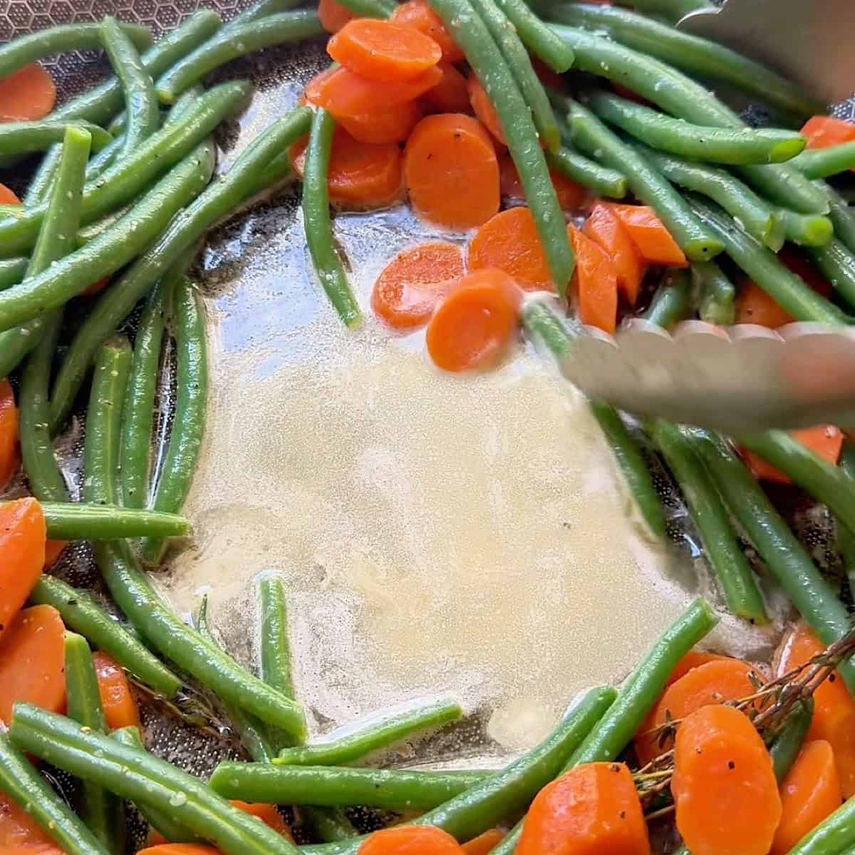 Vegetables surrounding thyme butter sauce in the middle of the pan.