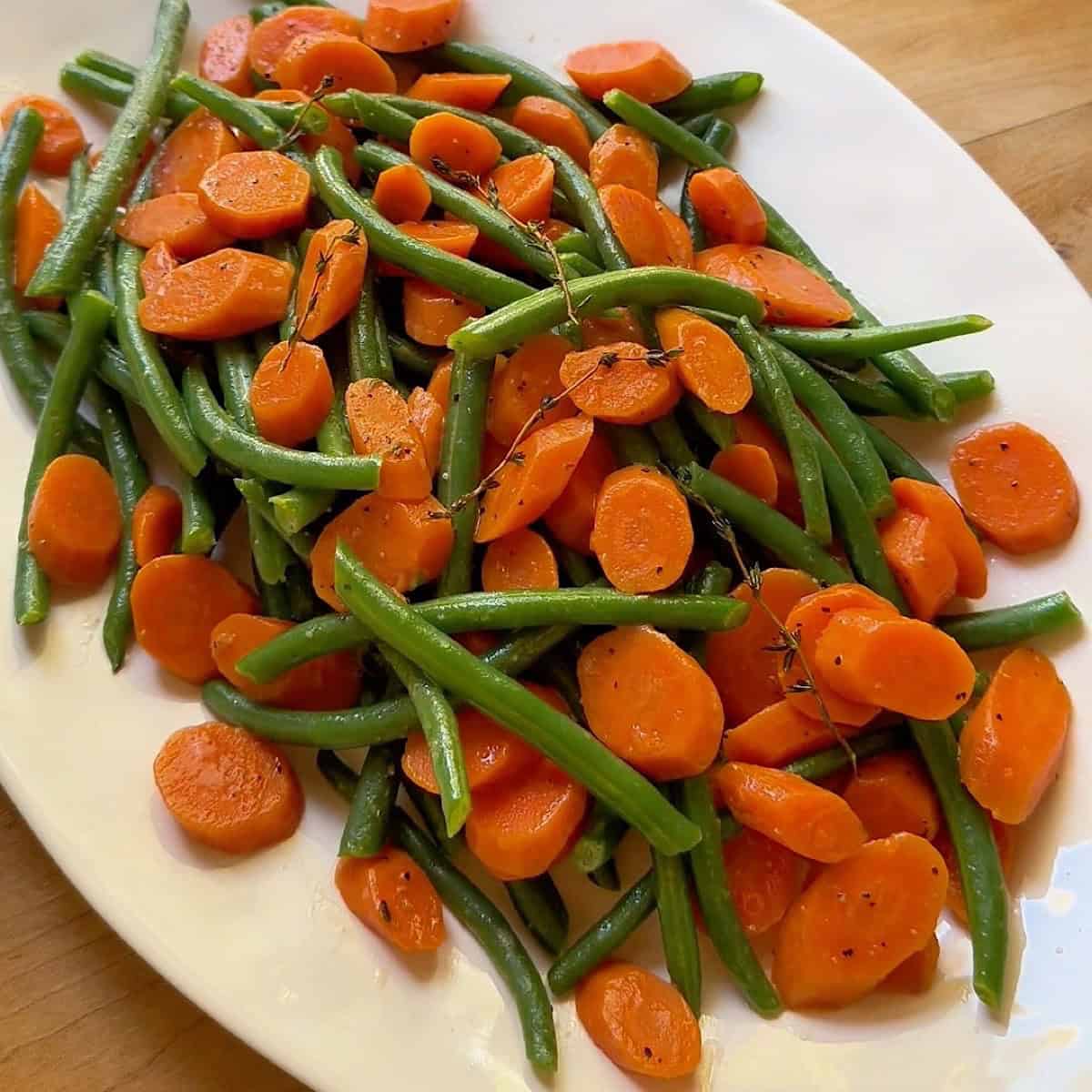 Green beans and carrots on a serving platter with thyme.