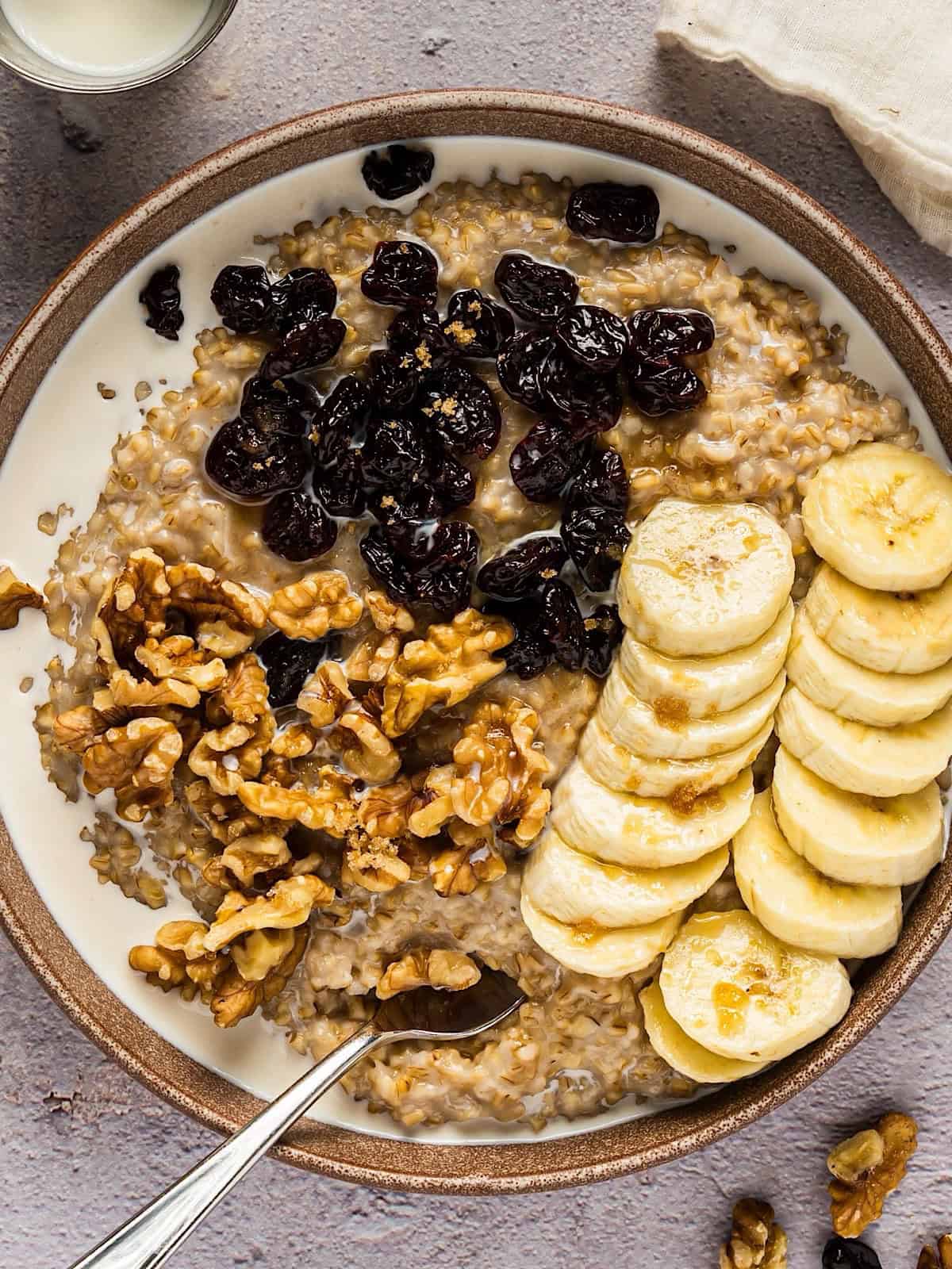 Creamy Instant Pot steel cut oats in bowl with toppings and linen nearby.